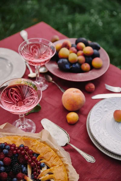 Tarta de bayas, frutas y copas de vino en la mesa en el jardín - foto de stock