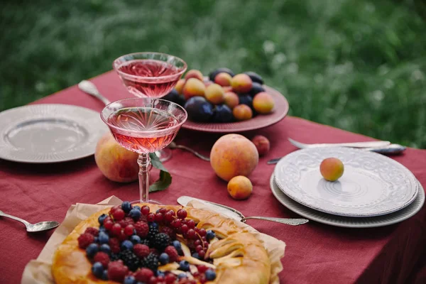 Delicious berries pie and glasses of wine on table in garden — Stock Photo