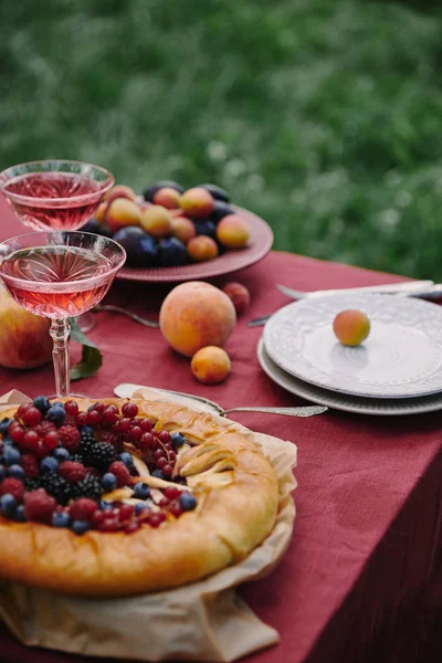 Yummy berries pie and glasses of wine on table in garden — Stock Photo