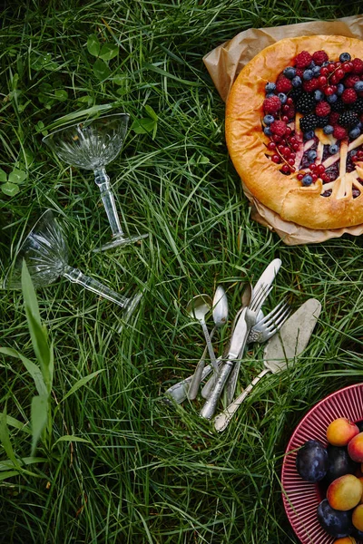 Vista dall'alto di torta con bacche, piatto con frutta e utensili su erba verde — Foto stock