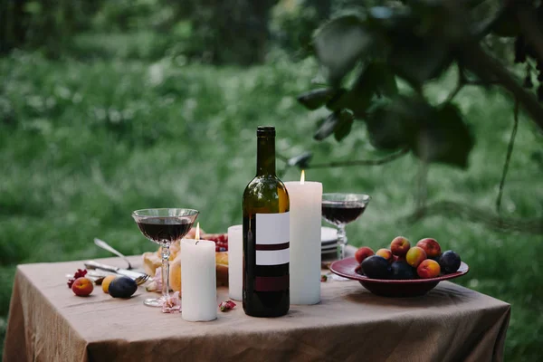 Velas, vino y frutas en la mesa en el jardín para la cena - foto de stock