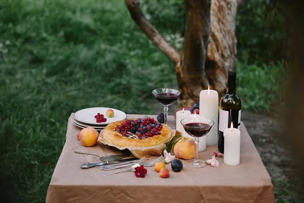 Velas románticas, vino y delicioso pastel en la mesa en el jardín - foto de stock