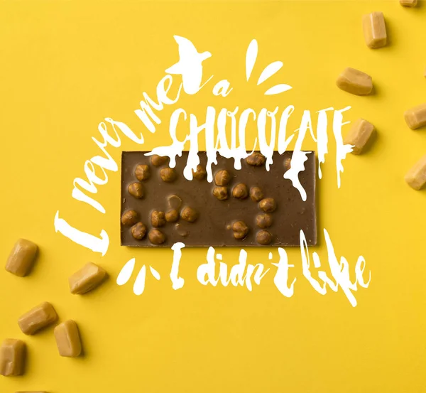 Vue du dessus de la barre de chocolat avec des bonbons au lait iris dispersés isolés sur jaune avec lettrage 
