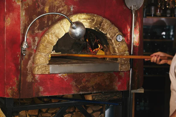 Plan recadré du chef mettant la pizza dans le four de maçonnerie à la cuisine du restaurant — Photo de stock
