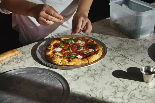 Cropped shot of woman spilling salt onto pizza margherita on marble tabletop — Stock Photo