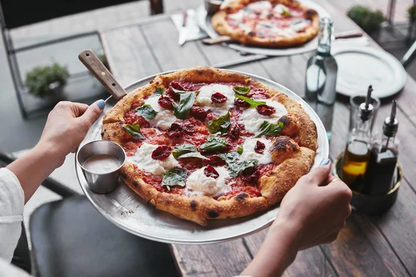 Tiro recortado de mujer llevando plato con sabrosa pizza para servir en la mesa en el restaurante - foto de stock