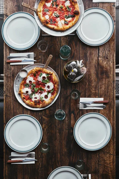 Top view of delicious pizza margherita on tray and plates on rustic table at restaurant — Stock Photo