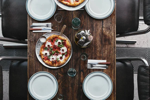 Top view of tasty pizza margherita on tray and plates on rustic table at restaurant — Stock Photo