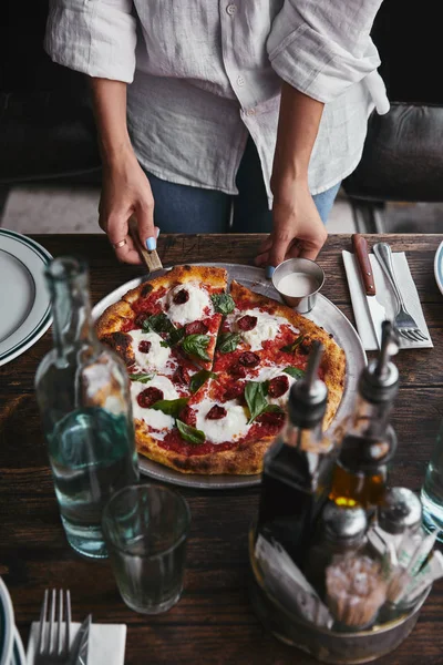 Cropped shot of serving delicious pizza on restaurant table with water — Stock Photo