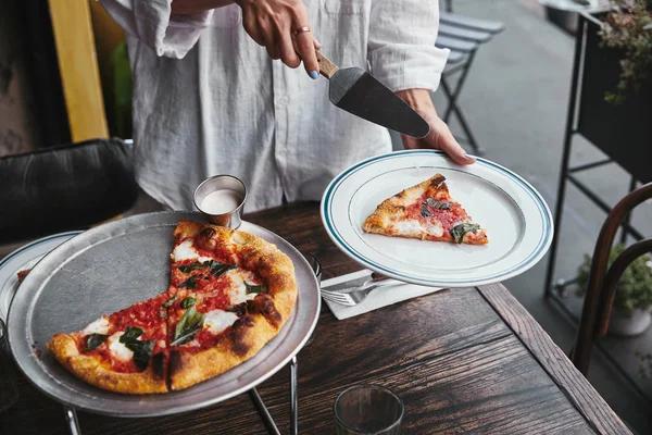 Tiro recortado de la mujer que sirve rebanada de pizza en el plato en el restaurante - foto de stock