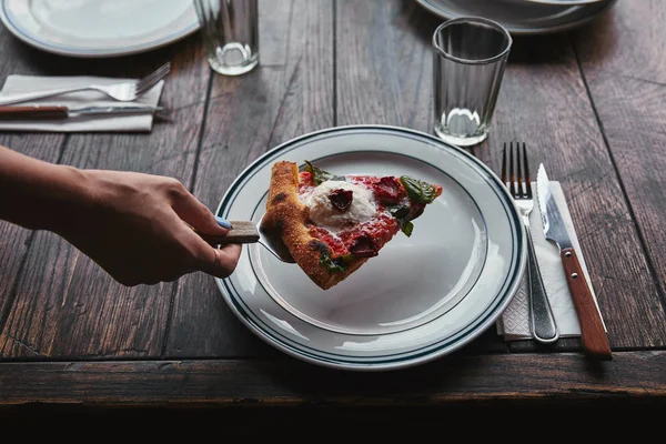 Tiro recortado de mujer sirviendo rebanada de pizza margherita en el plato en el restaurante - foto de stock