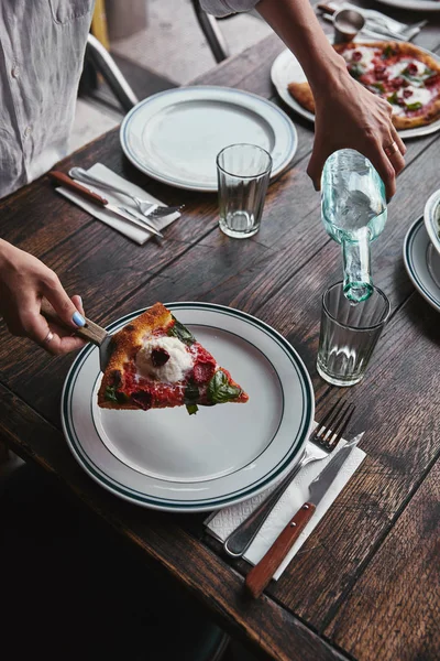 Plan recadré de la femme qui sert une tranche de délicieuse pizza margherita dans une assiette au restaurant — Photo de stock