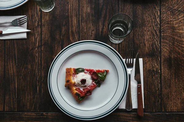 Top view of delicious slice of pizza on plate with setting on wooden table — Stock Photo