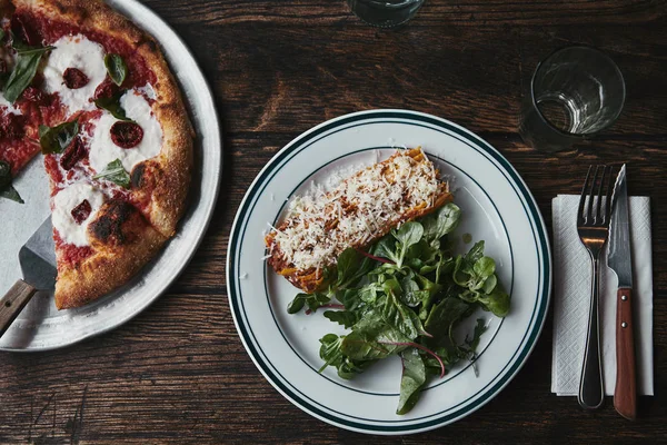 Vue de dessus de pizza fraîchement cuite et lasagne sur table en bois — Photo de stock