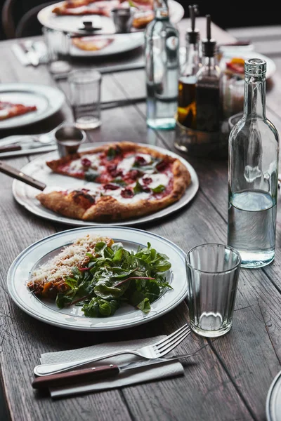 Close-up shot of delicious pizza and lasagne on wooden table with water — Stock Photo