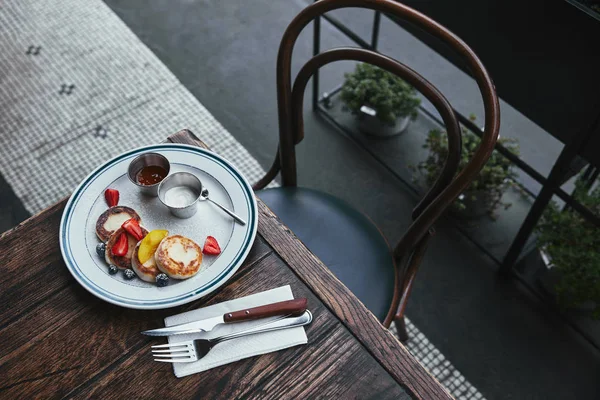 Tasty curd pancakes with bowls of dippings and cutlery on wooden table at restaurant — Stock Photo