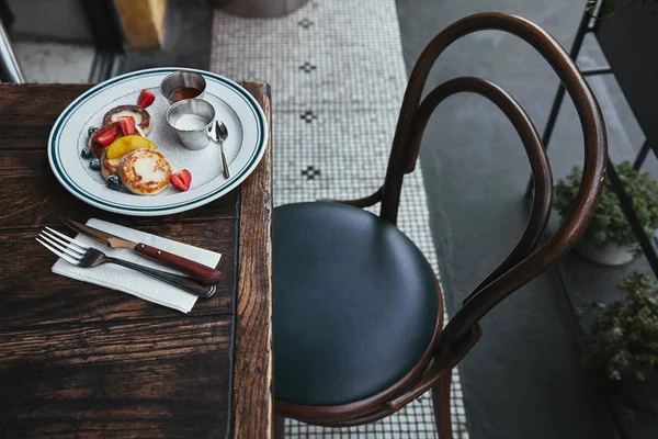 Delicious curd pancakes with bowls of dippings and cutlery on wooden table at restaurant — Stock Photo