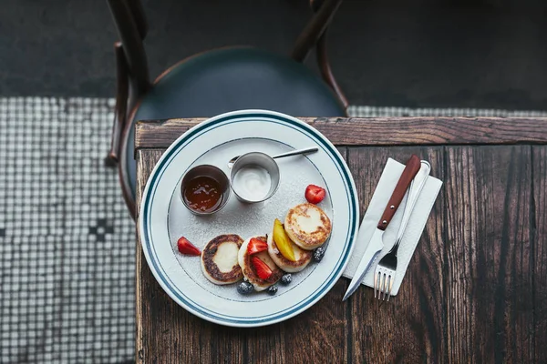 Top view of tasty cheese pancakes with bowls of dippings and cutlery on wooden table — Stock Photo