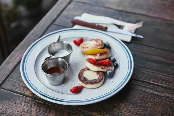 Close-up shot of tasty cheese pancakes with bowls of dippings and cutlery on wooden table — Stock Photo