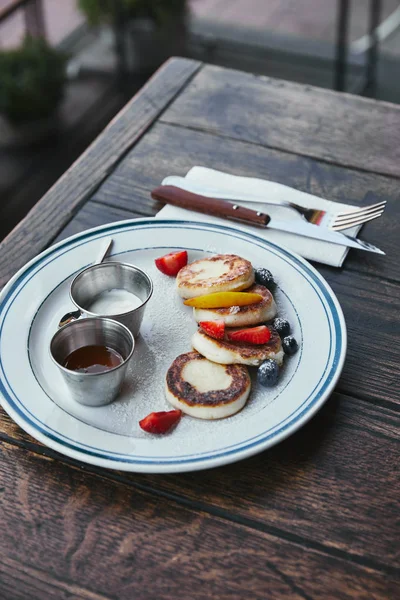 Close-up shot of delicious curd pancakes with bowls of dippings and cutlery on wooden table — Stock Photo