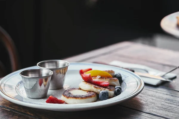 Close-up shot of delicious cheese pancakes with bowls of dippings on wooden table — Stock Photo
