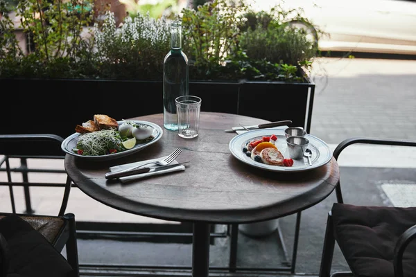 Delicious syrniki with salad and water bottle on table at restaurant — Stock Photo