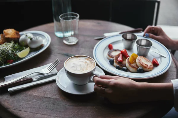 Foto recortada de mujer con tortitas de cuajada, ensalada y café en la mesa de madera en el restaurante - foto de stock