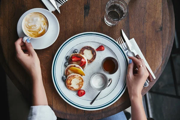 Plan recadré de femme avec de délicieux sironiki et café sur la table rustique au restaurant — Photo de stock