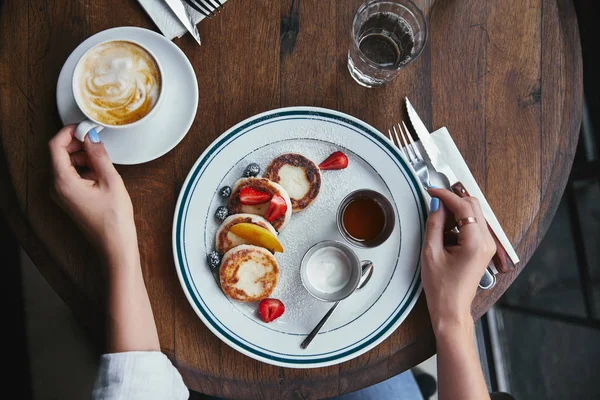 Cropped shot of woman with delicious syrniki and coffee on rustic table at restaurant — Stock Photo