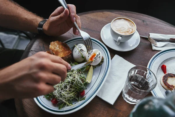 Tiro cortado de homem comendo salada com brotos e ovos no restaurante — Fotografia de Stock