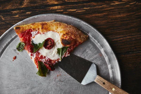 Vista superior de fatia de pizza com servidor em bandeja de metal e mesa de madeira — Fotografia de Stock