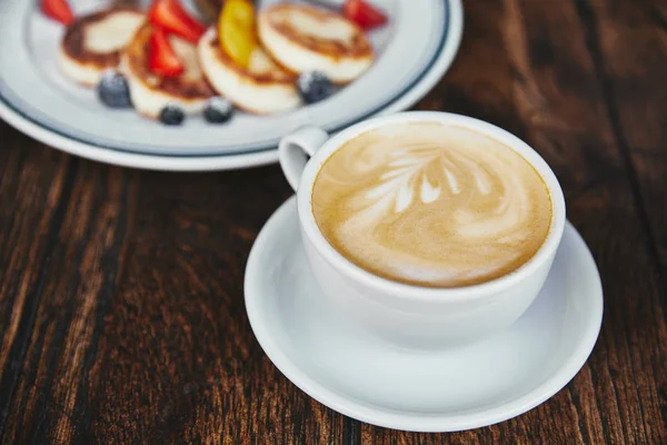 Крупным планом блины с сыром на тарелке и чашку кофе на деревенском деревянном столе — стоковое фото