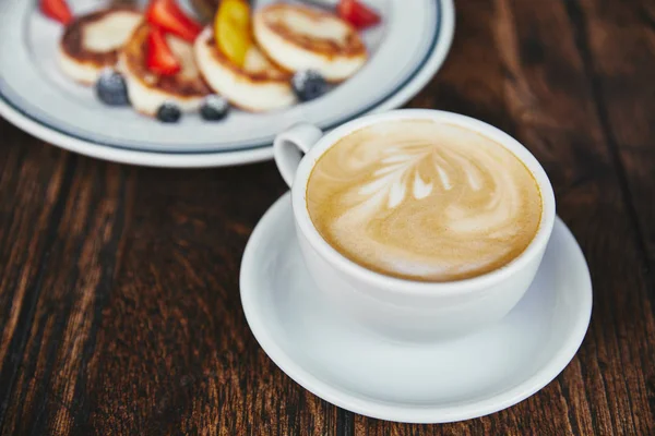 Close-up shot of tasty cheese pancakes on plate and cup of coffee on rustic wooden table — Stock Photo