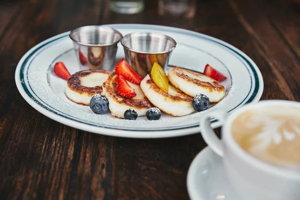 Köstliche Syrniki auf Teller und Tasse Kaffee auf rustikalem Holztisch — Stockfoto