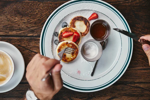 Recortado tiro de mujer comiendo delicioso syrniki en mesa de madera - foto de stock