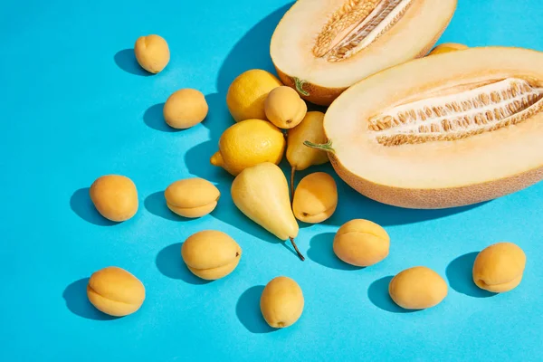 Vista de ángulo alto de deliciosas peras maduras, albaricoques, melón y limones en azul - foto de stock