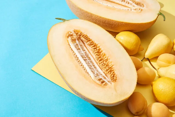 Primo piano vista di melone maturo dimezzato e pere fresche, limoni, albicocche su sfondo blu e giallo — Foto stock