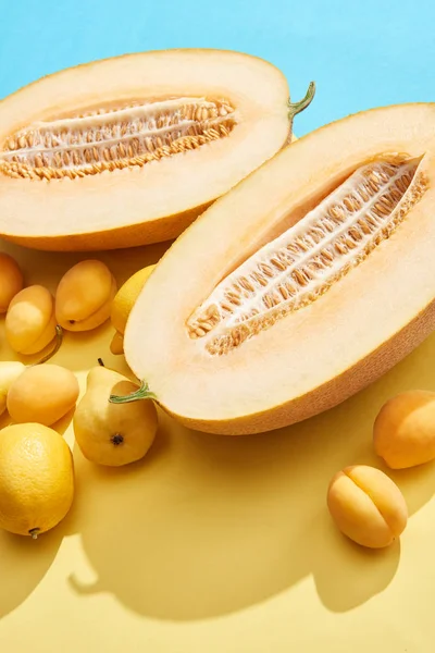 Nahaufnahme von frischen reifen halbierten Melonen, Zitronen, Aprikosen und Birnen auf blau und gelb — Stockfoto