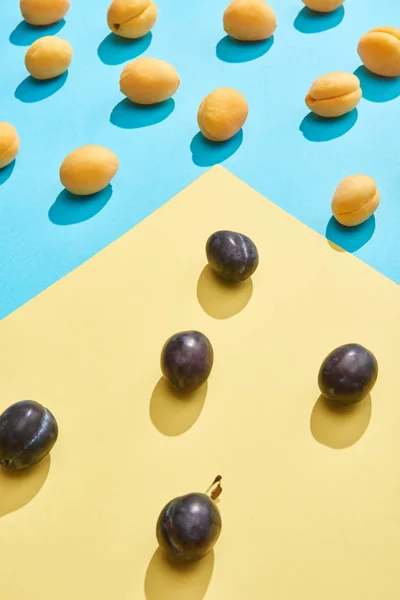 Vista de cerca de ciruelas dulces frescas y albaricoques sobre fondo azul y amarillo - foto de stock