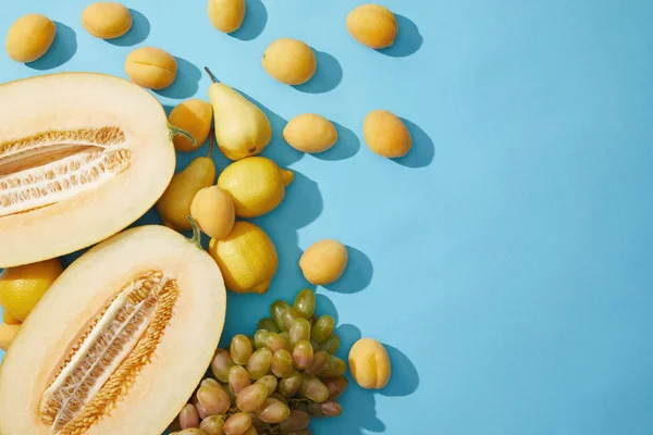 Vue de dessus de melon frais mûr, poires, abricots, citrons et raisins sur fond bleu — Photo de stock