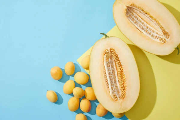 Draufsicht auf frische süße Aprikosen und halbierte Melone auf blauem und gelbem Hintergrund — Stockfoto