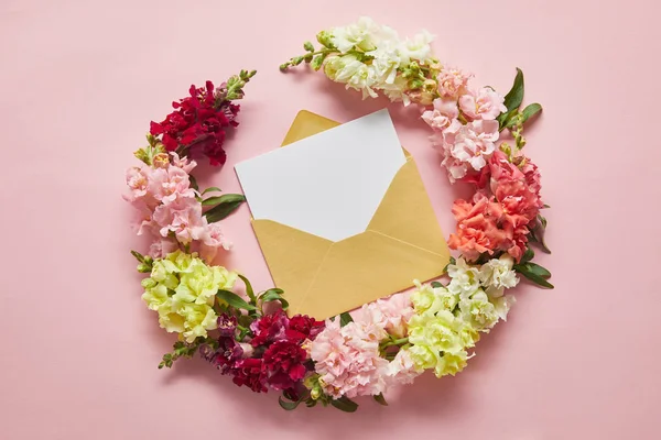 Vue du dessus de belles fleurs tendres et carte blanche dans une enveloppe rose — Photo de stock