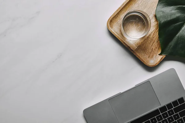 Laptop by wooden tray with glass of water on white marble background — Stock Photo