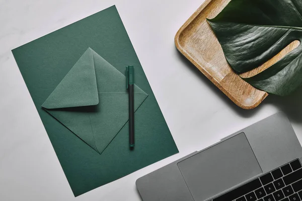 Зеленая бумага для письма шаблон на ноутбуке на белом мраморном фоне — стоковое фото