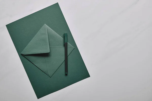 Green envelope with pen on white marble background — Stock Photo