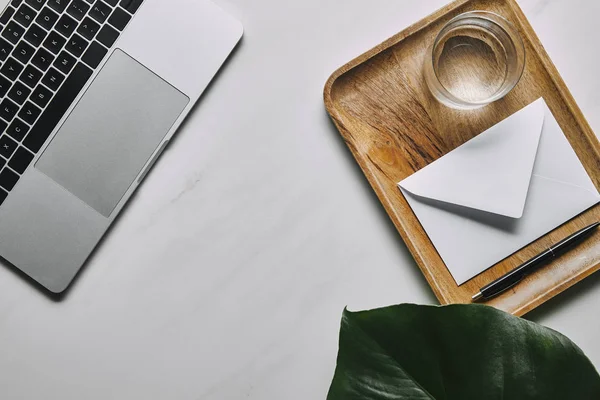 Laptop e bandeja de madeira com envelope e vidro sobre fundo de mármore branco — Fotografia de Stock