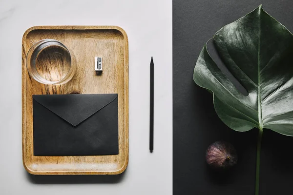 Glass of water and envelope in tray on white marble background with monstera leaf — Stock Photo