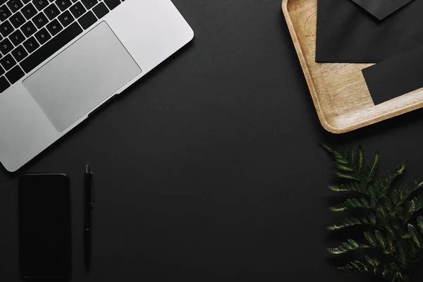 Smartphone e laptop em fundo preto com bandeja de madeira e folha verde — Fotografia de Stock