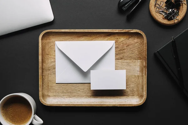 Flat lay with Wooden tray with empty business card and envelope on black background with laptop and stationery — Stock Photo