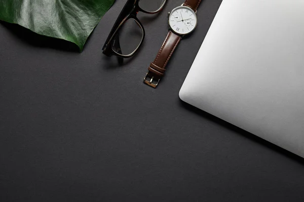Laptop com óculos e relógio no fundo preto com folha verde — Fotografia de Stock